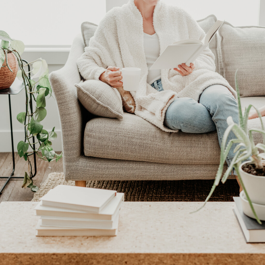 Woman sitting on a couch holding a book Woman sitting on a couch holding a book and coffee in a calm, light-filled living room.